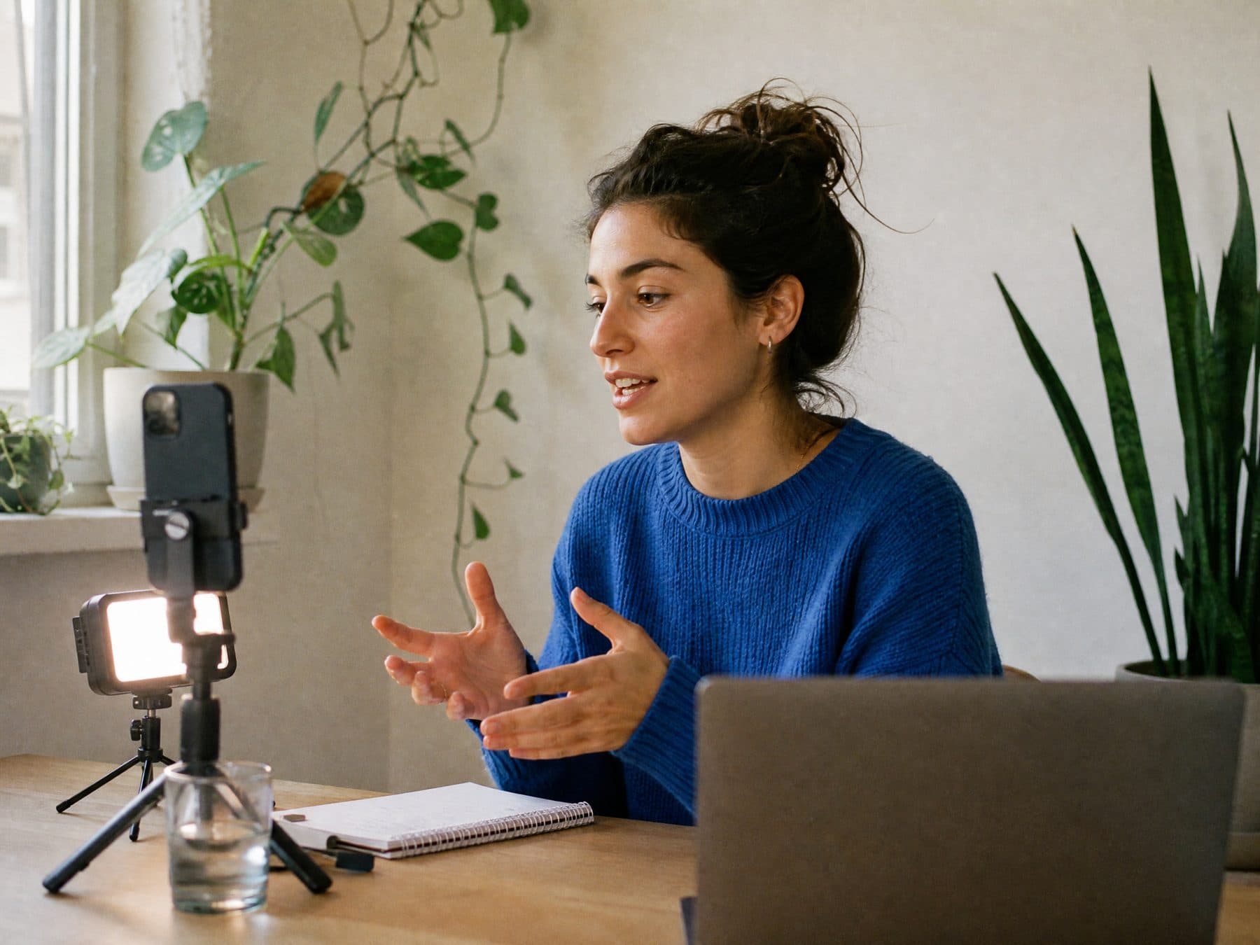 A content creator in a blue sweater filming herself with a phone on a small tripod